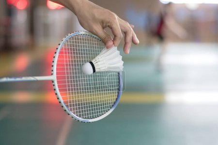 Badminton player holds racket and white cream shuttlecock in front of the net before serving it to another side of the court