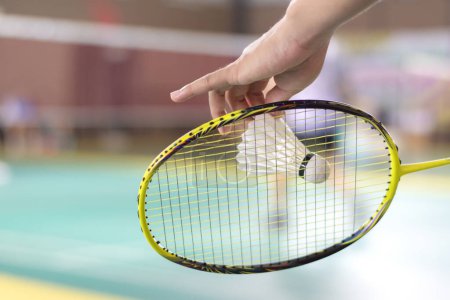 Badmintonspieler hält Schläger und weißen Federball vor das Netz, bevor er ihn auf eine andere Seite des Platzes serviert