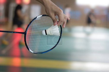 Téléchargez les photos : Le joueur de badminton tient une raquette et un volant blanc crème devant le filet avant de le servir sur un autre côté du terrain - en image libre de droit