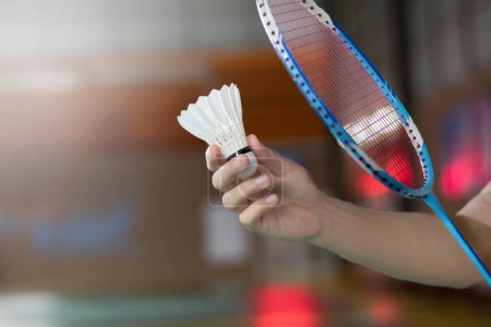 Badminton player holds racket and white cream shuttlecock in front of the net before serving it to another side of the court
