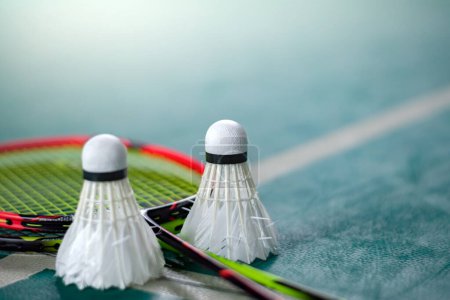 Téléchargez les photos : Navette de badminton blanc crème et raquette avec ombrage clair néon sur le sol vert dans la cour de badminton intérieure, fond flou de la cour de badminton, espace de copie. - en image libre de droit