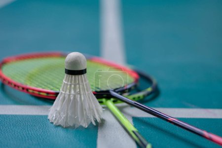 Photo for Cream white badminton shuttlecock and racket with neon light shading on green floor in indoor badminton court, blurred badminton court background, copy space. - Royalty Free Image