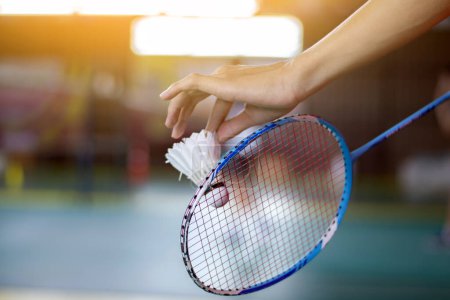 Badmintonspieler hält Schläger und weißen Federball vor das Netz, bevor er ihn auf eine andere Seite des Platzes serviert.