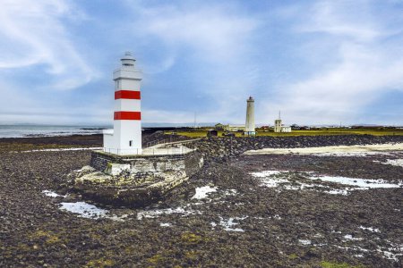 Neuer Leuchtturm in rot-weiß und alter Leuchtturm im Hintergrund bei Gardskagaviti bei Ebbe. Südliche Halbinsel, Island