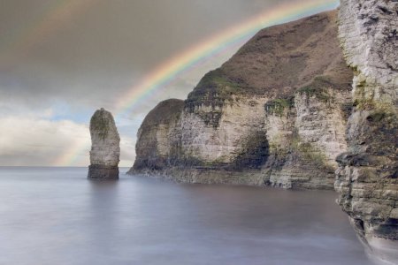 Los acantilados de Thornwick Bay cerca de Flamborough bajo un cielo oscuro con un arco iris, en Yorkshire, en la costa noreste del Mar del Norte en Inglaterra.