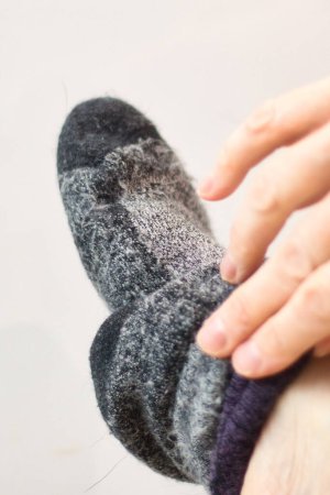 Téléchargez les photos : Doigts enlevant une chaussette grise sur un pied sur un fond blanc. - en image libre de droit