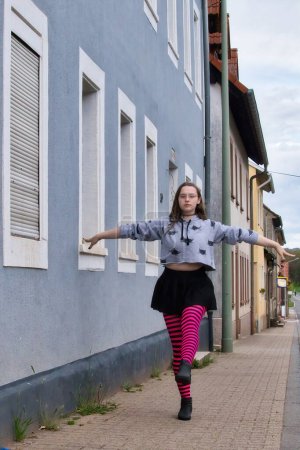 Téléchargez les photos : Lohnsfeld, Allemagne - Mai 16, 2021 : Adolescente en collants rose et noir équilibrant sur une jambe sur un trottoir sur la rue principale à Lohnsfeld, Allemagne. - en image libre de droit