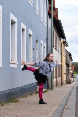 Téléchargez les photos : Lohnsfeld, Allemagne - Le 16 mai 2021 : Adolescente debout sur une jambe avec une jambe derrière elle sur un trottoir à Lohnsfeld, Allemagne. - en image libre de droit