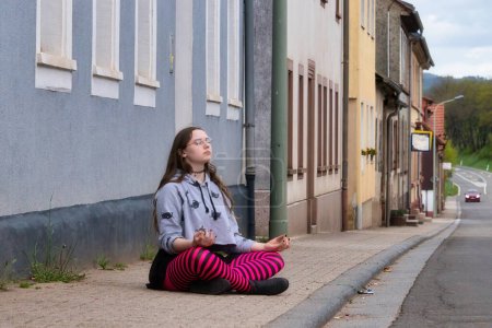 Téléchargez les photos : Lohnsfeld, Allemagne - 16 mai 2021 : Adolescente en collants roses et noirs méditant sur un trottoir à Lohnsfeld, Allemagne. - en image libre de droit