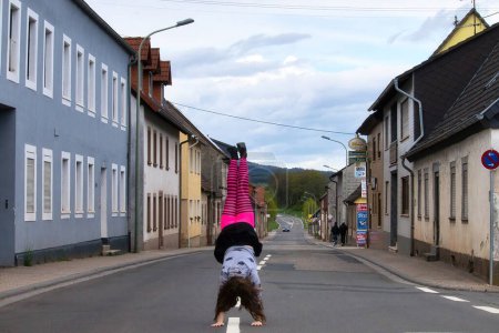 Téléchargez les photos : Lohnsfeld, Allemagne - Mai 16, 2021 : Adolescente en collants roses et noirs faisant un stand de main dans la rue à Lohnsfeld, Allemagne. - en image libre de droit