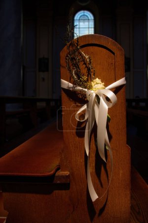 Weinheim, Germany - May 19, 2021: Sunlight shining on flower held on to the end of a pew with white ribbon in St. Laurentius Church in Weinheim, Germany.