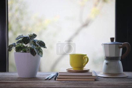 Photo for Yellow coffee cup and moka pot and plant pot in front of glass window - Royalty Free Image
