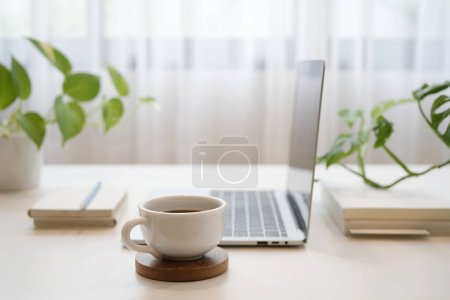 Photo for Coffee and laptop and notebooks and plants on wooden table in front of window - Royalty Free Image