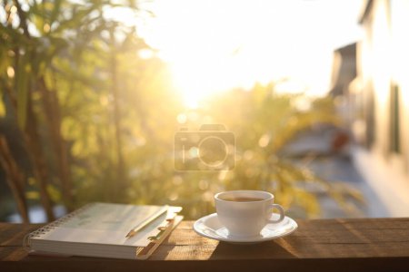 Foto de Coffee cup and notebook and plant pot on wooden table under sunlight - Imagen libre de derechos