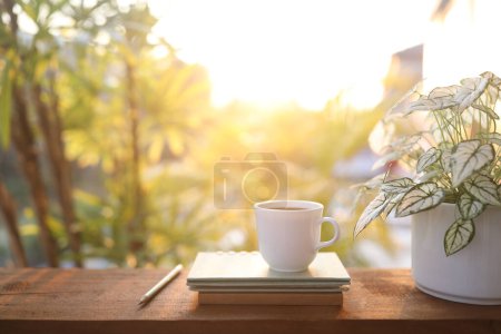 Kaffeetasse und Notizbuch und Engelsflügel auf Holztisch im Sonnenlicht