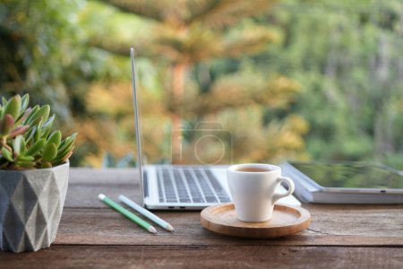 Laptop side view and coffee cup with notebooks on white table outdoor