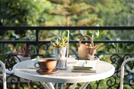 Teetasse und Teekanne aus Ton auf dem Balkon und Laptop-Seitenblick