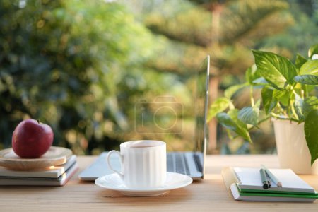 Eine Tasse Tee auf einem Holzarbeitstisch im Freien mit seitlichem Blick auf Laptop und Notebooks Balkon im Freien