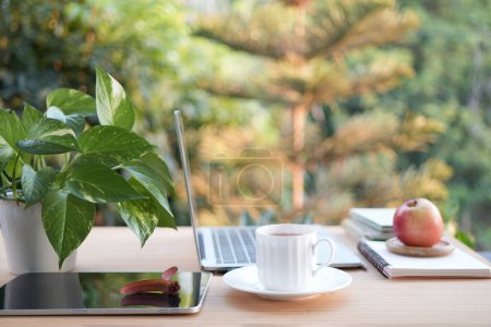 Une tasse de thé sur une table de travail en bois à l'extérieur avec vue latérale sur ordinateur portable et ordinateurs portables balcon extérieur