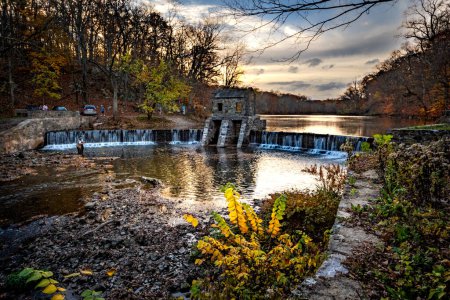 Photo for Morristown, NJ - USA - Nov 5, 2022 An autumnal horizontal wide angle view of New Jersey's historic stone Speedwell Dam during sunset. Fly fisherman in the foreground and people hiking in the distance. - Royalty Free Image