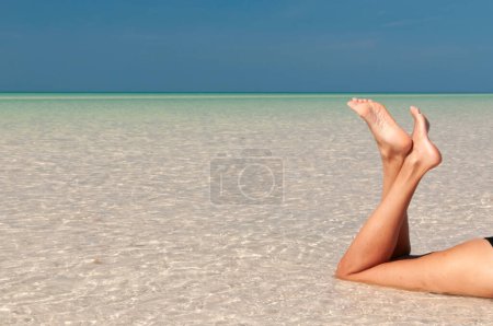 Foto de Detalle de las piernas de una mujer acostada en el agua en una playa, vacaciones de ensueño en la isla tropical de Holbox en México. - Imagen libre de derechos