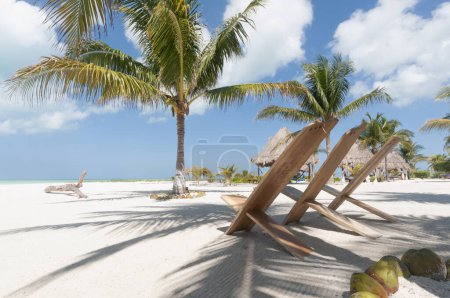 Foto de Sillas rústicas en la playa de arena blanca en los trópicos con palmeras contra el cielo azul. Isla Holbox, México. Concepto de viaje de vacaciones - Imagen libre de derechos