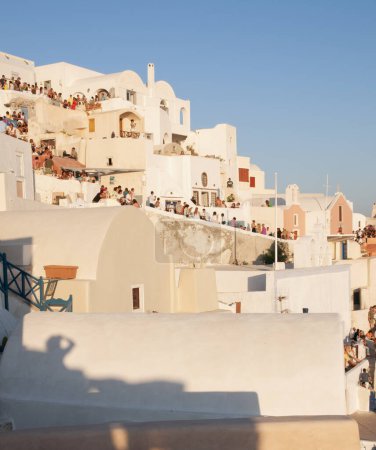 Téléchargez les photos : Coutume traditionnelle dans le village d'Oia en Grèce que tout le monde rassemble sur les toits des maisons dans un moment de détente et de convivialité pour admirer le coucher de soleil sur la mer Égée - en image libre de droit