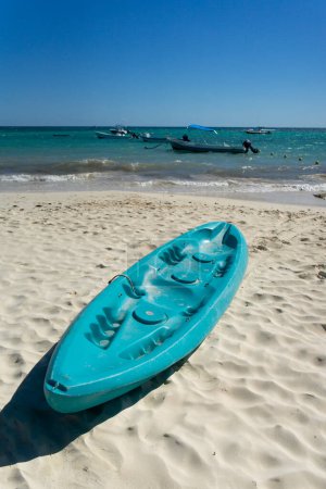 Tropical beach in Mexico with turquoise kayaks on white sand, blue sky and calm sea with boats in the background. Ideal place for vacation sports and relaxation