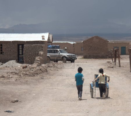 Foto de Dos jóvenes emprendedores conducen un carro de refrescos hacia un SUV lleno de turistas en un viaje por el Altiplano de Bolivia. El trabajo infantil es una parte de la vida en lugares como la pequeña y luchadora aldea de Colchani. - Imagen libre de derechos