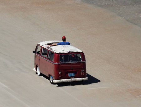 Foto de Mini furgoneta retro cruzando en arena dura con un hombre viendo los eventos a su alrededor. - Imagen libre de derechos