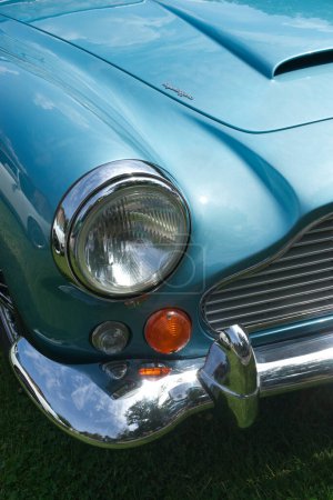 Foto de Primer plano en la parte delantera de un Aston Martin DB IV azul, Serie IV de 1962. Parte de la capucha, el faro y el parachoques están por verse. Luz solar. - Imagen libre de derechos
