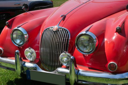 Téléchargez les photos : Red Jaguar XK 150 SE OTS automobile de 1958. Détails avant montrant la mascotte Jaguar, le logo du nom, le gril, les feux de voiture et le pare-chocs. En plein air, lumière du soleil. - en image libre de droit