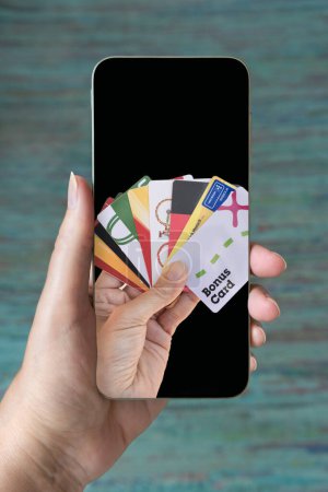 Téléchargez les photos : Les cartes de fidélité sont affichées à l'écran d'un téléphone portable tenu par une main. Espace de copie. - en image libre de droit