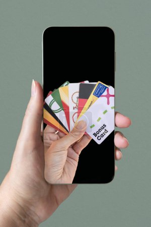 Photo for Fidelity cards are shown on the screen of a mobile phone held by a hand. Copy space. Green-cyan background. - Royalty Free Image