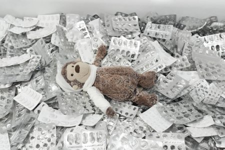 Foto de Un mono de juguete blando con vendajes está acostado en una pila de blisters vacíos. - Imagen libre de derechos