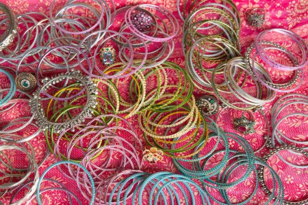 Indian or Pakistani traditional Chura bracelets made out of aluminum or nickel silver and some rings. Items placed on a colorful textile cloth.
