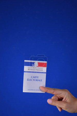 Téléchargez les photos : Une main tenant une carte de vote française. Fond texturé bleu. Espace de copie. - en image libre de droit
