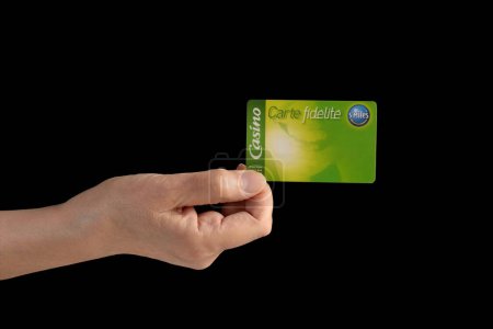 Photo for A hand holding a payback fidelity card from a French supermarket. Isolated on a black background. - Royalty Free Image