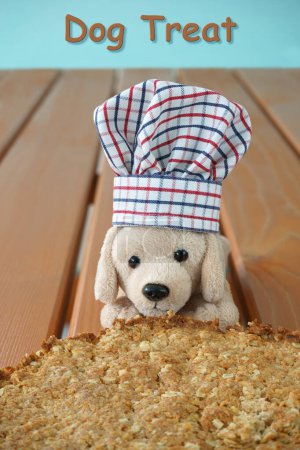 Photo for A soft toy dog wearing a chef cook hat behind a home-baked unsweetened cake. Dog treat written as text. Butter, Oatmeal, Coconut flakes, butter and flour are the ingredients. - Royalty Free Image