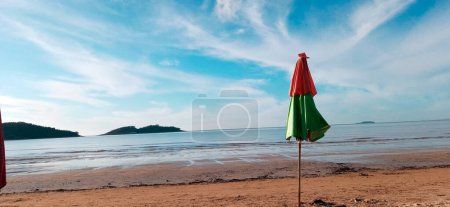 Téléchargez les photos : Parapluie, Parasol sur la plage de Piuma avec ciel bleu, sable foncé, eaux de marée basse et îles en arrière-plan. Espirito Santo, Brésil. L'un des sites touristiques les plus fréquentés sur la côte sud de l'État d'Esprito Santo, région du sud-est du Brésil. - en image libre de droit