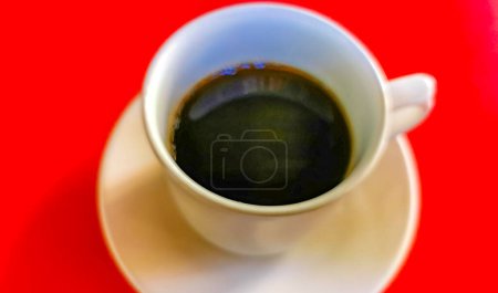 Foto de Taza de café negro americano con cuchara y plato sobre fondo de mesa roja comida y bebida en el restaurante en Zicatela Puerto Escondido Oaxaca México. - Imagen libre de derechos