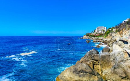 Foto de Agua azul turquesa y extremadamente hermosa olas grandes surfistas rocas acantilados piedras montañas y rocas en la playa en Zicatela Puerto Escondido Oaxaca México. - Imagen libre de derechos