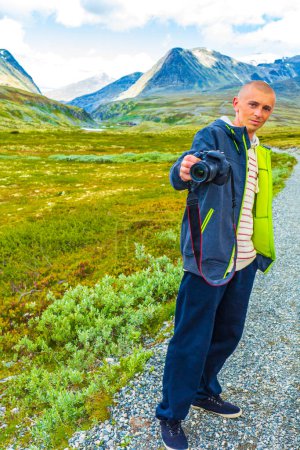 Young hiker traveler photographer with camera and beautiful summer landscape panorama with mountains river lake rocks and hiking trail of Rondane National Park in Ringbu Innlandet Norway in Scandinavia.