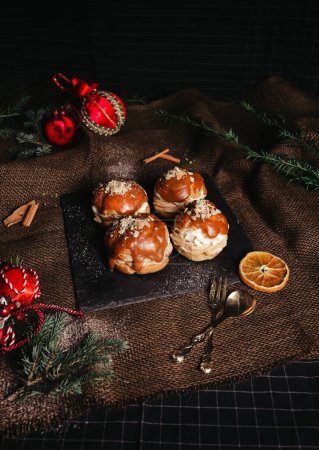Photo for Profiteroles with white creme and christmas decoration on dark background. Vintage photo of tasty dessert with caramel - rustic style. - Royalty Free Image