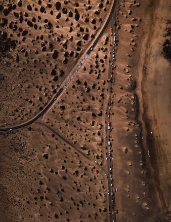 Photo for Aerial vieiw of road with parked cars on the side in dry sand dunes. Top view  - vertical photo of sand beach on the coast with vehicles on the road. - Royalty Free Image