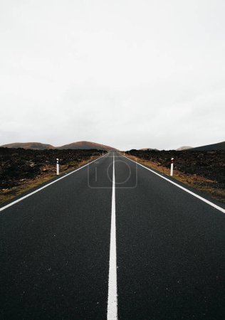 Photo for Vertical image of empty road with perfect symmetric lines at overcast day. Travel shot from trip of Lava island - Lanzarote (Canary Islands). - Royalty Free Image