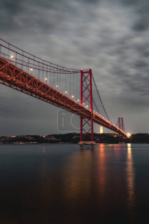 Photo for Vertical image of the 25 April bridge (Ponte 25 de Abril) located in Lisbon, Portugal, crossing the Targus river at night. - Royalty Free Image