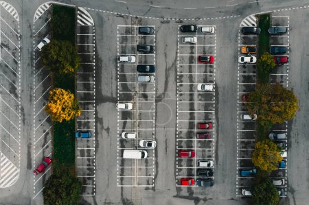 Parking et voitures colorées garées entre les lignes d'en haut (vue de dessus) - fond en béton gris. Parking avec des arbres colorés en automne.