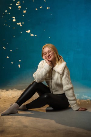 Photo for Blonde cute caucasian woman in white fur sweater on blue background. Fake Snow is flowing all over her. She is happy, celebrating christmas and new year. Studio portrait - Royalty Free Image