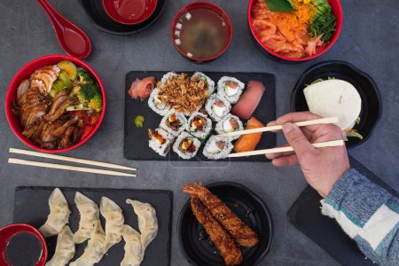 Téléchargez les photos : Manger des sushis. Restaurant japonais, assortiment de sushis. Gros plan de la main avec des baguettes roulantes avec fond rustique. - en image libre de droit